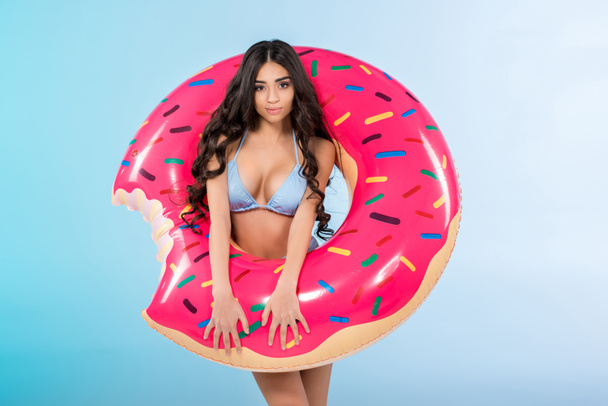 attractive stylish girl posing with inflatable donut ring, isolated on blue  - Fotó, kép