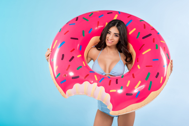 beautiful girl posing with trendy inflatable donut ring, isolated on blue  - 写真・画像