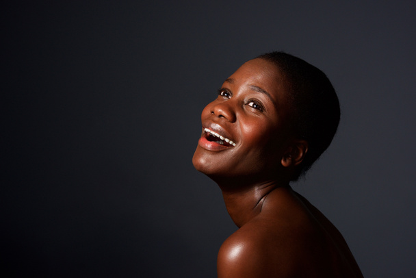 Close up portrait of happy young african woman with naked shoulders laughing on gray background - Valokuva, kuva