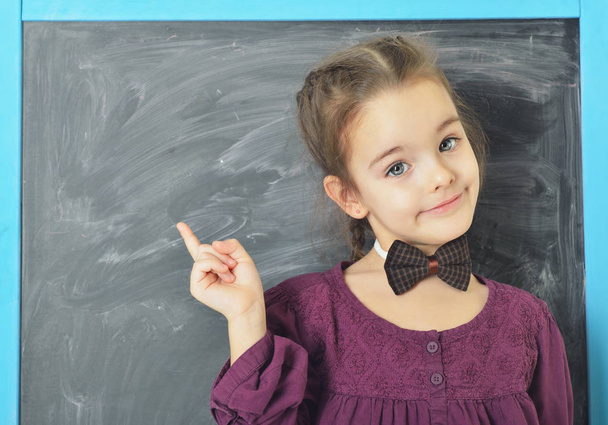 Schattig liitle meisje permanent in de buurt van blackboard, glimlachend en wijzen  - Foto, afbeelding