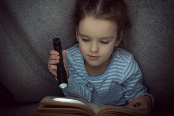 Bambina che legge fiabe libro sotto le coperte alla vigilia
 - Foto, immagini