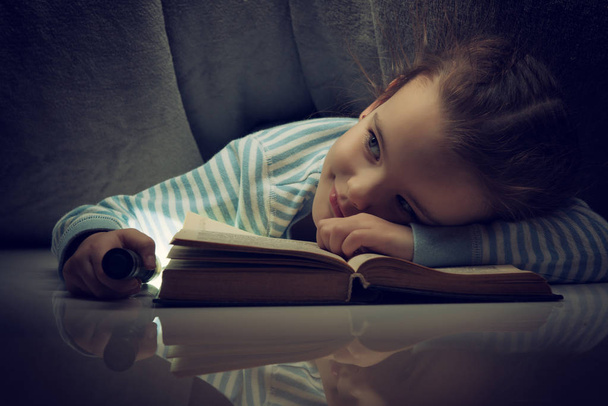 Menina lendo contos de fadas livro sob as capas na véspera
 - Foto, Imagem