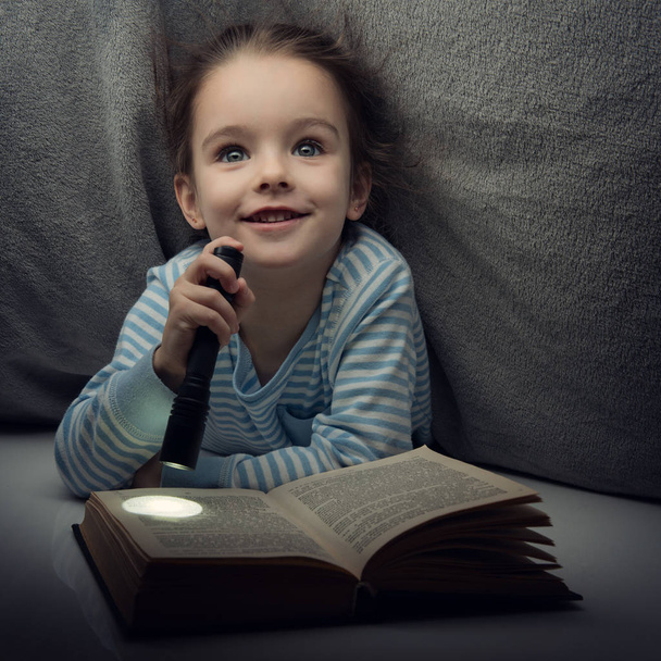Маленька дівчинка читає казкову книгу під обкладинками напередодні
 - Фото, зображення