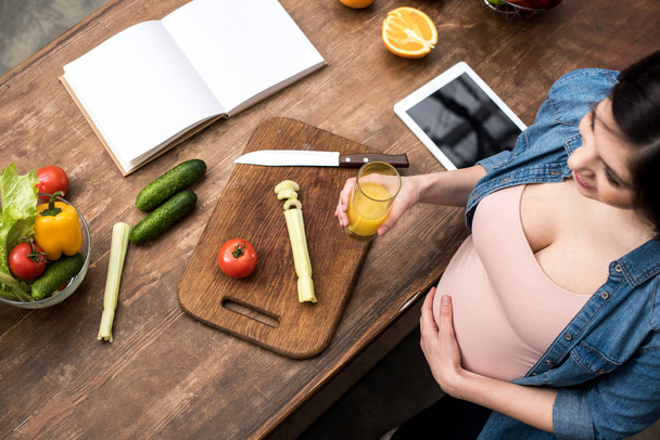 overhead view of pregnant woman holding glass of fresh juice while cooking - Foto, immagini