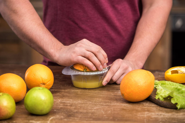 обрезанный снимок молодого человека, выжимающего свежий апельсиновый сок дома
 - Фото, изображение