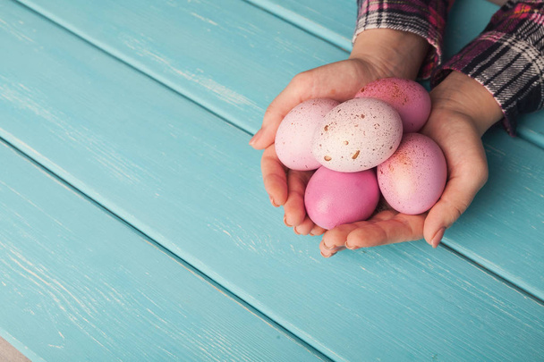 Woman holding pink colored easter eggs on blue table - Valokuva, kuva