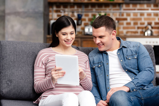 sonriente joven embarazada pareja usando digital tablet juntos en casa
 - Foto, Imagen