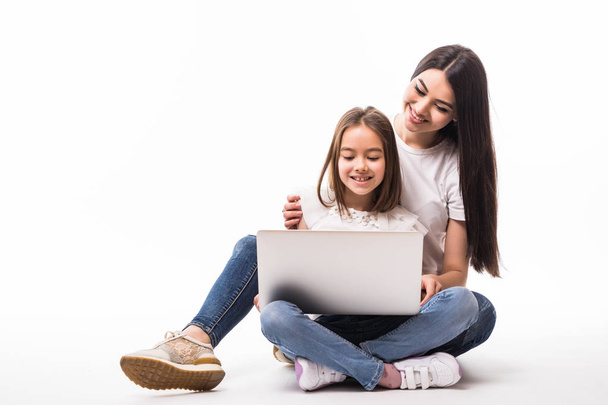 Dcera matka a úsměvem sleduje na obrazovce přenosného počítače sedí na podlaze na bílém pozadí - Fotografie, Obrázek