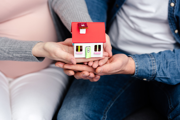 close-up partial view of young pregnant couple holding small house model - Foto, imagen