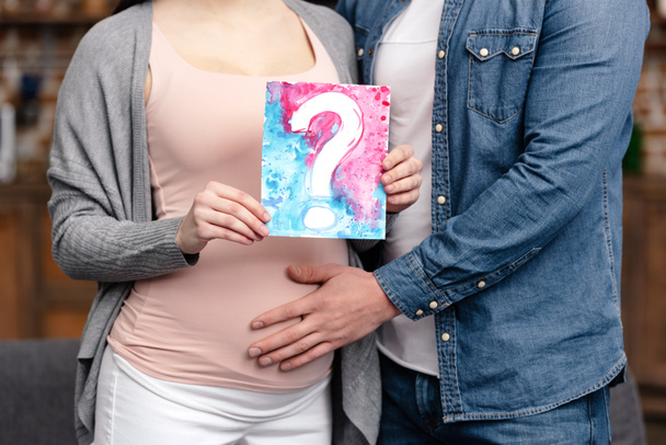 cropped shot of young pregnant couple holding bright card with question mark - Fotoğraf, Görsel