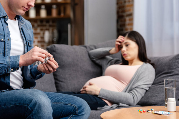 colpo ritagliato di uomo in possesso di pillole mentre la donna incinta malata sdraiata sul divano
 - Foto, immagini