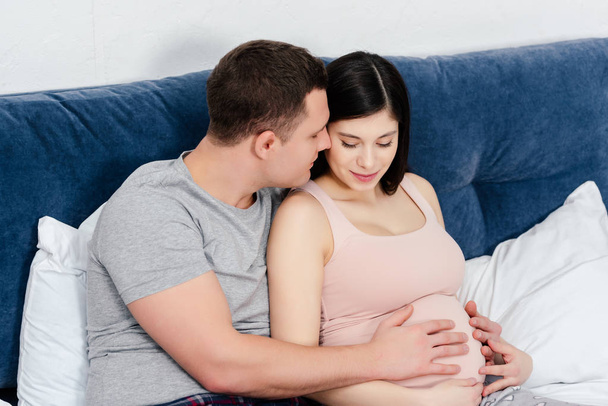 happy young pregnant couple touching belly together on bed - Fotoğraf, Görsel