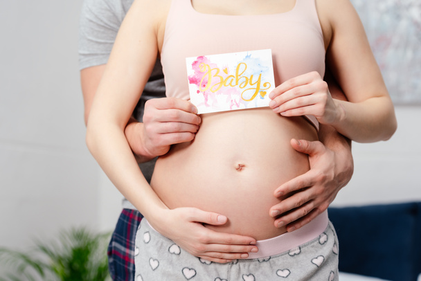 Schnappschuss von schwangerem Paar, das Karte mit Wort Baby hält - Foto, Bild