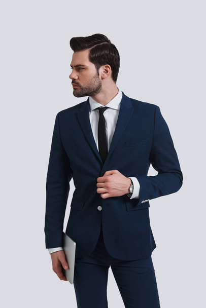 good looking young man in suit adjusting his jacket and looking away in studio  - Фото, изображение