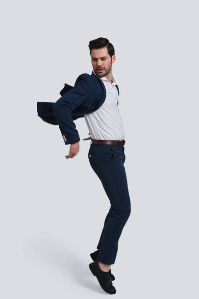 full length of handsome young man in full suit making a face while jumping against grey background - Foto, Bild