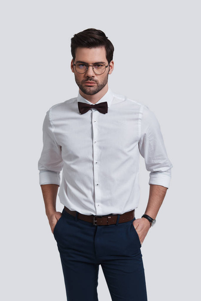 young businessman with bow tie keeping hands in pockets and posing in studio - Photo, Image