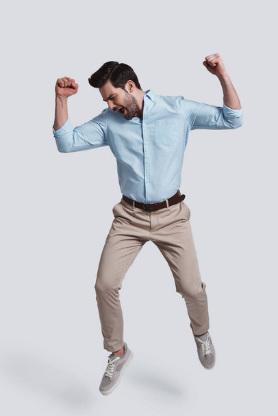 full length of handsome young man gesturing success and shouting while jumping grey background - Фото, зображення