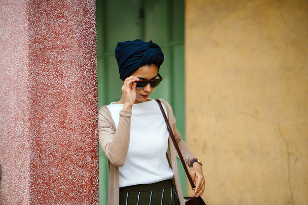 Portrait of a young Muslim woman (Islam) in sunglasses wearing a turban (headscarf, hijab). She is elegant, attractive and professionally dressed. - Foto, Imagen