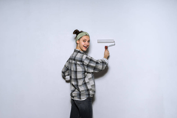 girl in plaid shirt colors the wall with a roller - Fotó, kép