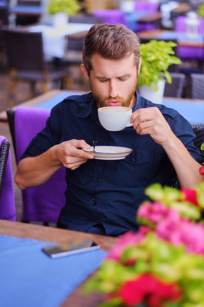 Venkovní záběr hezký vousatý muž oblečený v neformálním oblečení s šálkem kávy. - Fotografie, Obrázek