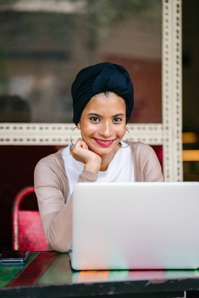 Retrato de una joven y atractiva mujer musulmana (asiática, árabe, malaya) empresaria o empresaria que trabaja en su portátil. Ella está vestida con inteligencia y lleva un turbante (hijab, pañuelo para la cabeza) y está sentada
. - Foto, Imagen