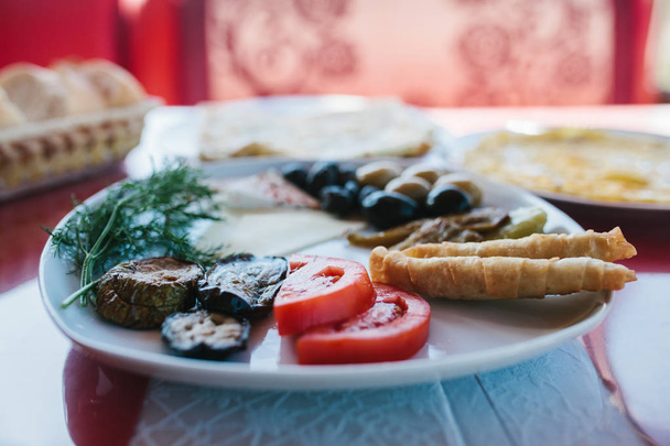 Primer plano. Desayuno en un plato compuesto por tomate, queso, rollo, aceitunas negras y verdes y berenjena
. - Foto, Imagen