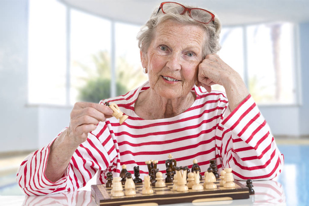 Senior oude vrouw Schaken, verplaatsen van stukken over het schaakbord op grote glazen achtergrond - Foto, afbeelding