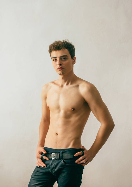 A yoA young, handsome guy posing with a gnawed torso, demonstrating a sports body, muscles, relief, a pumped-up body. Background white wall. Shooting with natural light, minimal retouching - Фото, зображення
