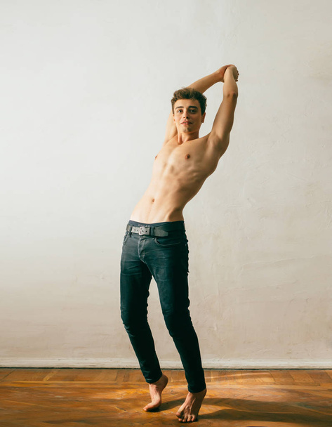 A yoA young, handsome guy posing with a gnawed torso, demonstrating a sports body, muscles, relief, a pumped-up body. Background white wall. Shooting with natural light, minimal retouching - Photo, image