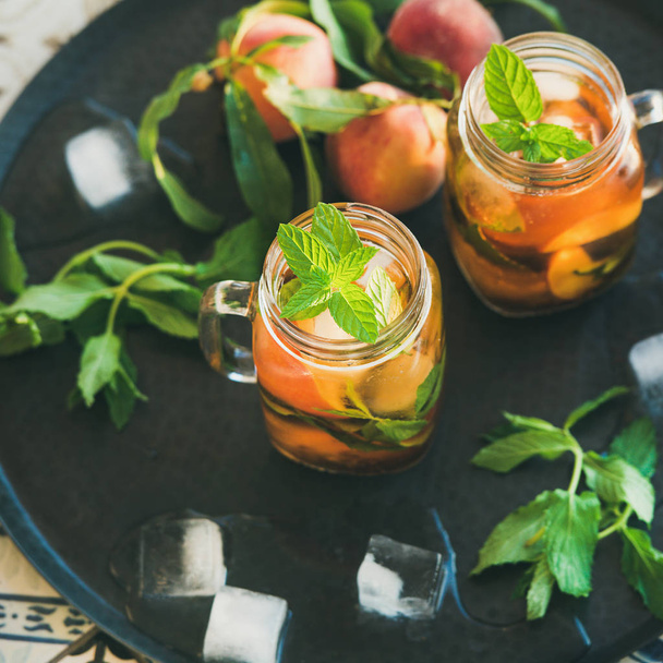 Summer refreshing cold peach ice tea with fresh mint in glass jars on metal tray over colorful oriental ceramic tile background - Φωτογραφία, εικόνα
