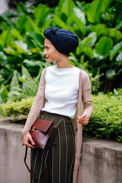Portrait of a young Muslim woman walking down a path in a park in the city. She is wearing a turban (hijab) and is tall, elegant and beautiful. The woman is of Malay, Asian or Saudi descent. - Photo, Image