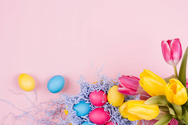 Fondo festivo de Pascua de primavera: huevos multicolores pintados en casa, ramo de tulipanes sobre fondo rosa claro pastel, vista superior, espacio para copiar
. - Foto, Imagen