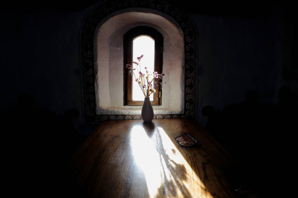 Μια ανθοδέσμη πάνω στο τραπέζι στις ακτίνες του ένα φωτεινό sunin ένα σκοτεινό δωμάτιο, φως του ήλιου, διαπερνά μέσα από ένα στενό παράθυρο πέφτει σε ένα ξύλινο τραπέζι. Το μπουκέτο είναι πάνω στο τραπέζι για το φωτισμό. - Φωτογραφία, εικόνα