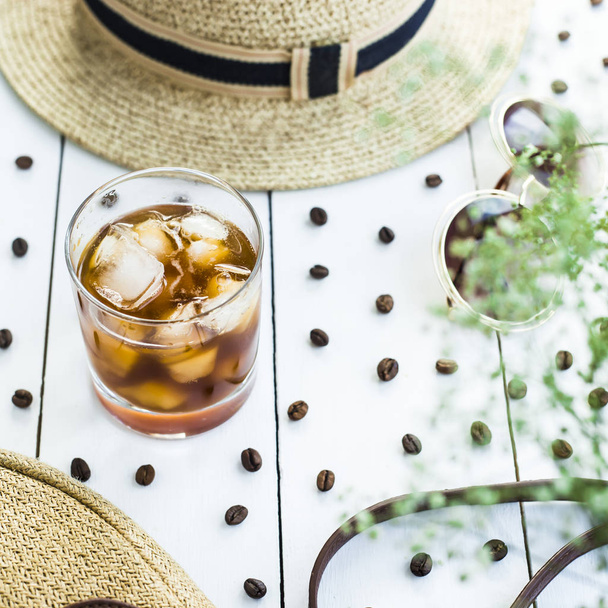 Cold coffee in a glass with ice. On the table among coffee beans and summer women's accessories. Summer relax concept - Foto, imagen