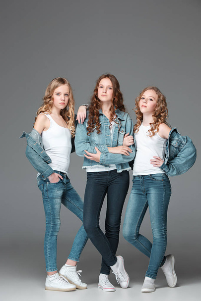 The fashion girls standing together and looking at camera over gray studio background - Fotografie, Obrázek