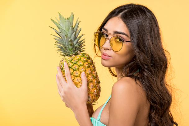 beautiful girl in sunglasses holding fresh pineapple, isolated on yellow - 写真・画像