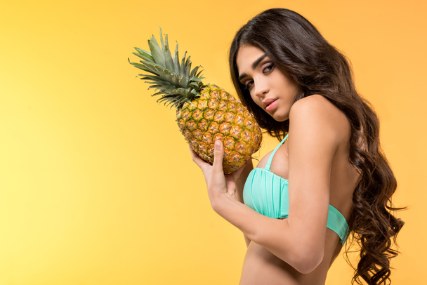 beautiful girl in bikini holding fresh pineapple, isolated on yellow - Fotó, kép