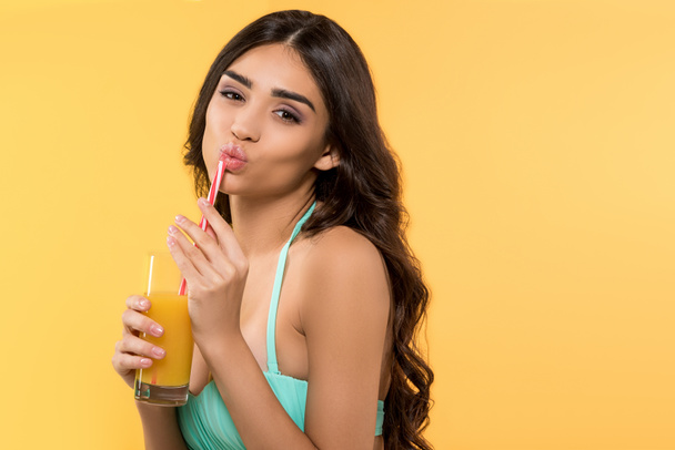 beautiful young woman posing in bikini with glass of juice, isolated on yellow - Фото, изображение