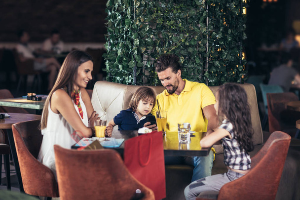  Familie mit zwei Kindern vergnügt sich nach dem Einkaufen in einem Café - Foto, Bild