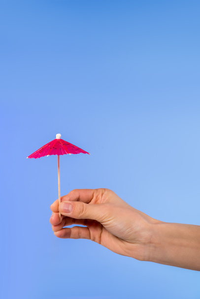 cropped view of female hand with cocktail umbrella, isolated on blue - Fotografie, Obrázek