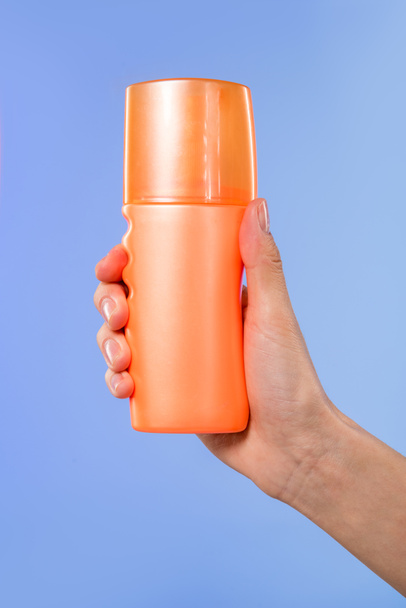 cropped view of female hand with bottle of sunscreen, isolated on blue - 写真・画像