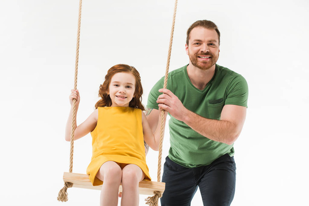 Smiling father riding little daughter on swing isolated on white - Zdjęcie, obraz