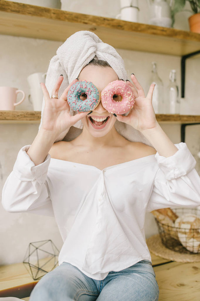 Playful young woman holding donuts against her eyes and smiling - Fotoğraf, Görsel