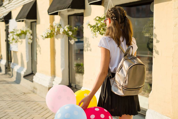 Vista trasera. Chica adolescente estudiante de secundaria con globos, en uniforme escolar va por la calle de la ciudad
 - Foto, imagen