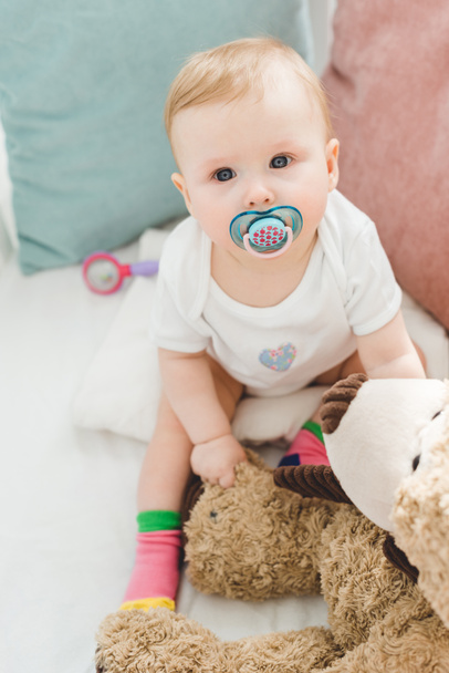 High angle view of infant with baby dummy and teddy bear sitting in crib - Foto, Imagem