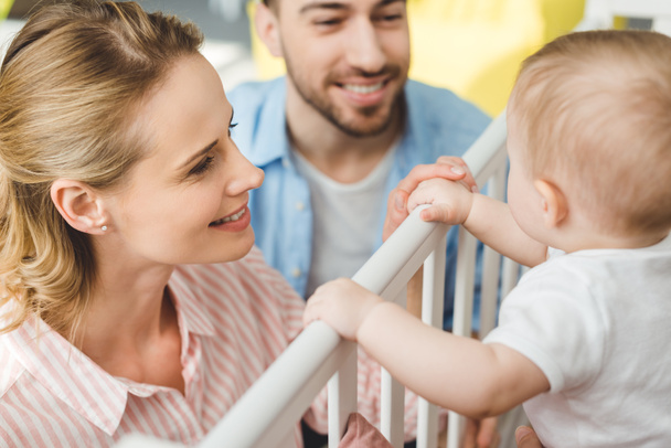 Young parents playing with infant daughter standing in crib - Photo, Image
