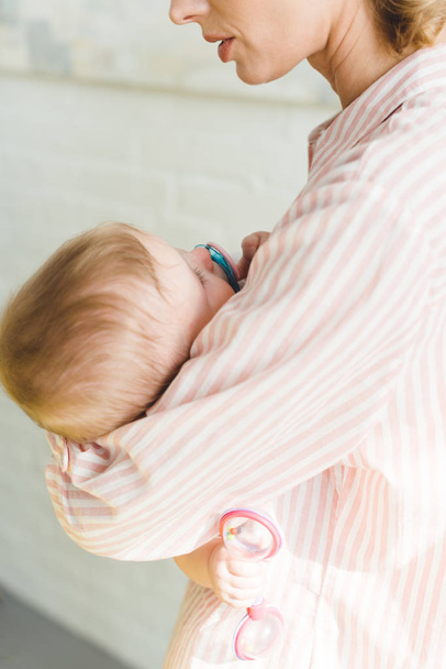 Cropped view of mother holding infant daughter with baby dummy and toy  - Foto, Imagen
