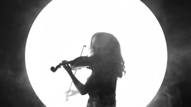 Fragmento de vídeo preto e branco de uma linda garota tocando violino em um fundo círculo branco na fumaça
. - Filmagem, Vídeo