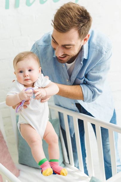 feliz padre sosteniendo bebé hija con juguete en cuna
 - Foto, imagen
