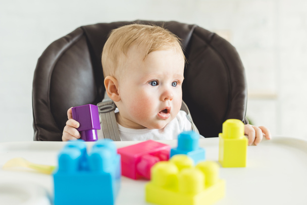 Adorable bébé sititng dans une chaise de bébé avec des blocs en plastique
 - Photo, image
